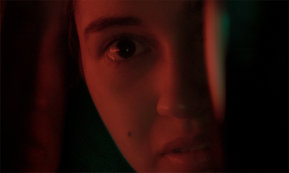 Extreme close-up of a person's eyes and nose under heavy red lighting.