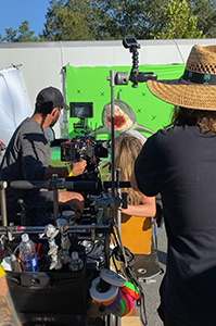 Film crew operating a camera and equipment in front of a green screen with a shark prop.