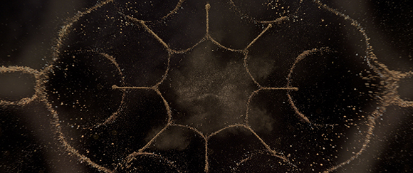 Golden shimmering particles forming a symmetrical, web-like pattern against a dark background.