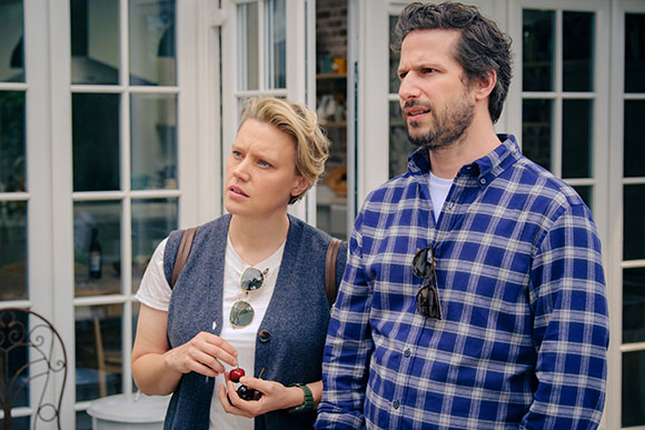 A woman in a blue vest and a man in a blue plaid shirt looking away with serious expressions.