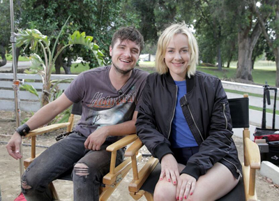 A man in a grey t-shirt and a woman in a black bomber jacket sit in wooden director's chairs.