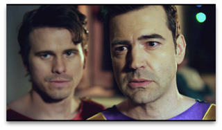 Two men with serious facial expressions looking toward the camera in a dimly lit setting.