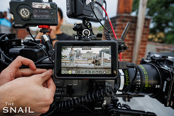 Hands adjusting a professional video camera equipped with a monitor and various electronic accessories.