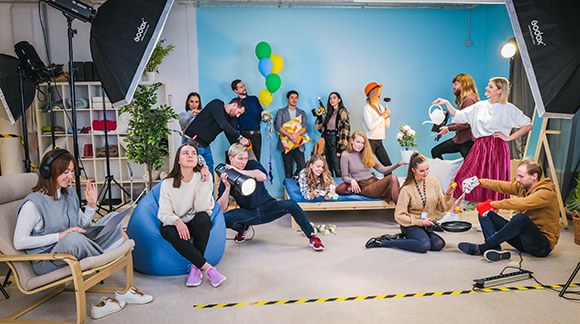 A diverse group of people posing in a blue studio with softbox lights and studio equipment.