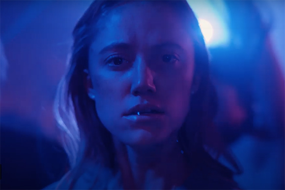 A woman looks forward with a serious expression under intense blue lighting.