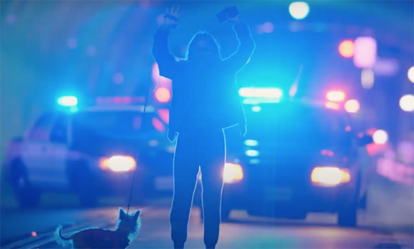Silhouette of a person with arms raised standing between two police cars with bright blue and red flashing lights.