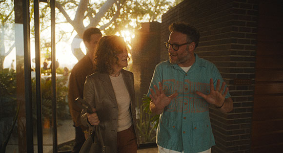 Three people stand outdoors near a brick building during a golden sunset.