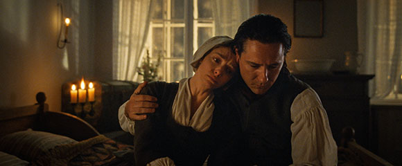 A woman leans her head on a man's shoulder as they sit together in a candlelit room.