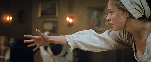 A woman in period clothing reaches her hand out toward something off-camera with a distressed expression.