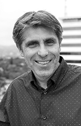 Black and white close-up portrait of a middle-aged man with short hair smiling at the camera.