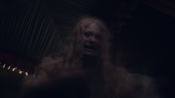 A blurry, low-light shot of a person with long, light-colored hair in a dark setting.