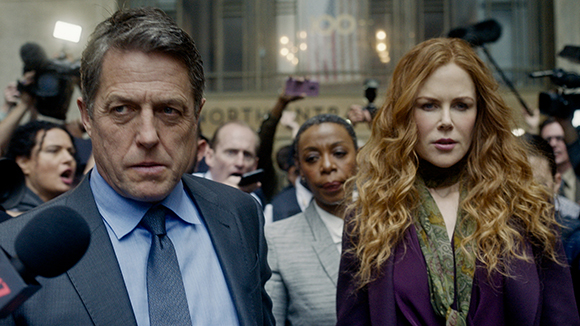 A man in a suit and a woman with long red hair walk through a crowd of reporters and cameras.
