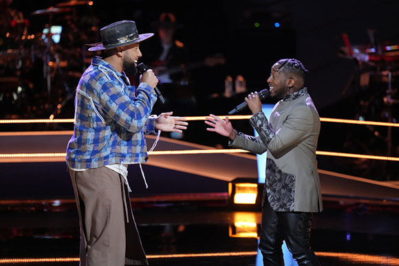 Two men facing each other on a stage, holding microphones and singing.