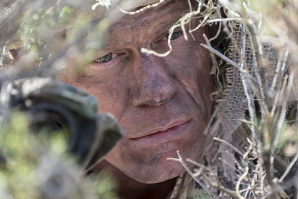 A person with face paint looking through branches and camouflage netting.