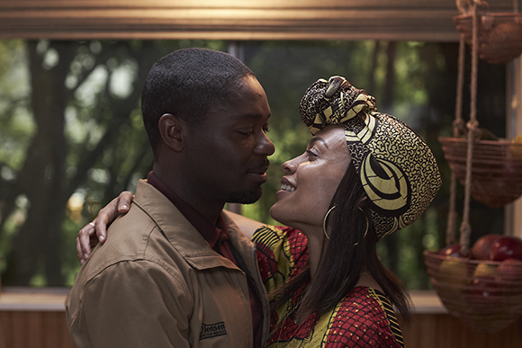 A man and a woman in colorful clothing look into each other's eyes and smile closely.