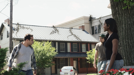Three young people stand outdoors near a large tree and a multi-story building.
