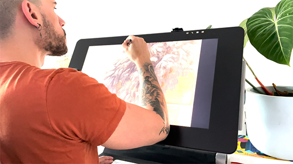 A person's arm and hand using a stylus to draw on a large digital tablet screen.