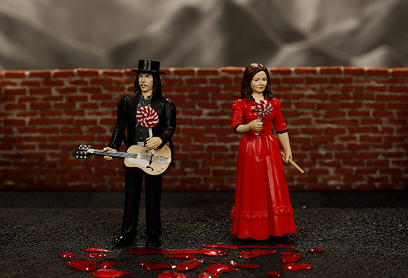 Figurines of a man in black with a guitar and a woman in a red dress holding a red lollipop.