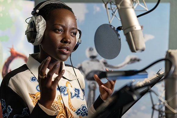 A person wearing headphones speaks into a professional microphone in a studio setting.