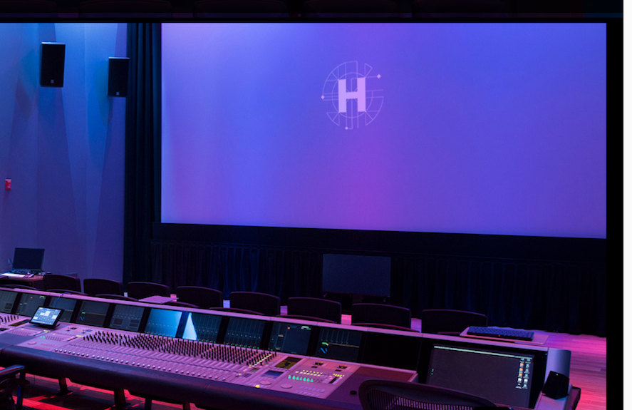 A large blue projection screen with a white circular logo in a dark room with a control console in the foreground.