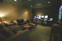 A lounge with a dark leather sofa, coffee table, and a workspace with multiple computer monitors.