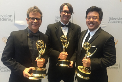 Three men in formal attire smiling and holding gold Emmy awards against a Television Academy backdrop.