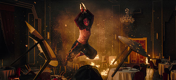 A person in mid-air jumps through a dark, chaotic room filled with flying sparks and broken furniture.