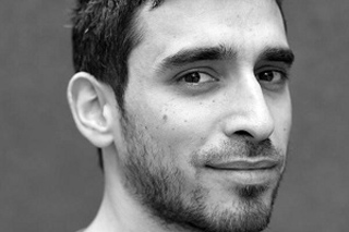 Black and white close-up portrait of a man with dark hair and a short beard looking toward the camera.