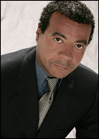 A man with short dark hair wearing a dark suit, blue shirt, and patterned tie looking forward.