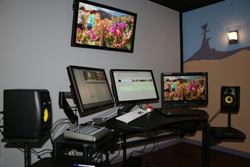Video editing setup with three computer monitors, studio speakers, and a mixing console on a black desk.