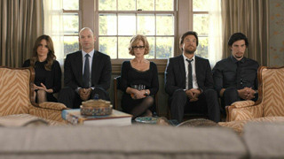 Five people in formal attire sit in a row against a large window in a living room.
