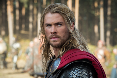 A man with long blonde hair and a beard wearing dark armor and a red cape in a forest.