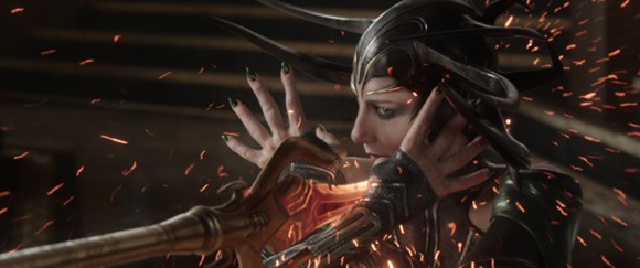 A woman with dark horns and black nail polish holds a staff amidst flying sparks.