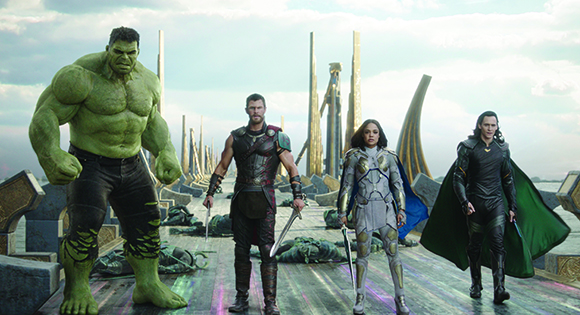 The Hulk, Thor, Valkyrie, and Loki standing on a platform against a sky with golden pillars.
