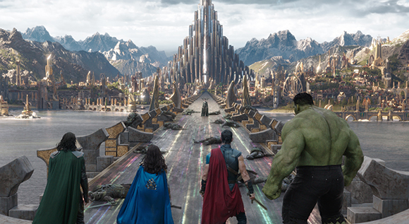 Four characters stand on a bridge facing a sprawling golden city and a tall central palace.