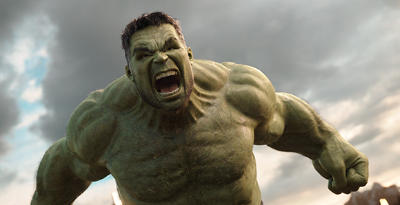 A muscular green humanoid creature with a fierce expression roaring against a cloudy sky.