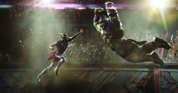 A large green muscular figure and a smaller armored figure leap toward each other in a crowded arena.