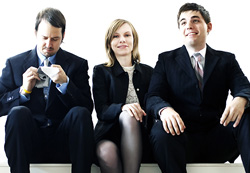 Three people in dark business suits sitting against a white background.