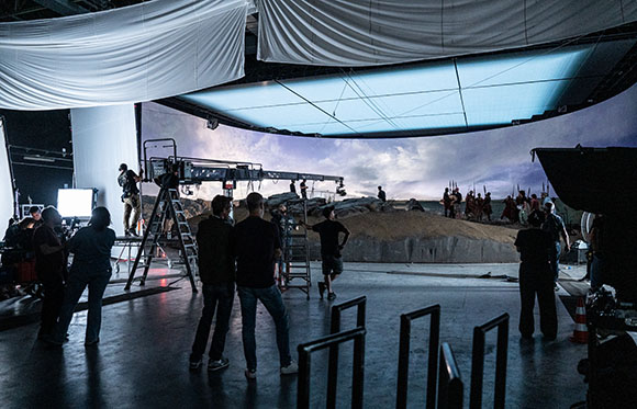 Film crew in a studio using a large LED screen to display a landscape for virtual production.