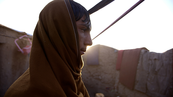 A person wrapped in a brown cloth looks toward the light in a sunlit outdoor setting.
