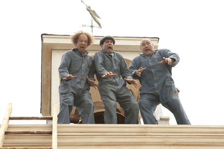 Three men in blue jumpsuits stand on a roof with shocked facial expressions and outstretched hands.