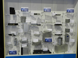 A wall display case with multiple shelves holding various electronic devices, including hard drives, routers, and other compu