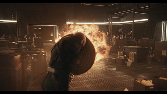 A person in dark clothing is surrounded by a large, bright explosion of fire in a dark, industrial room.