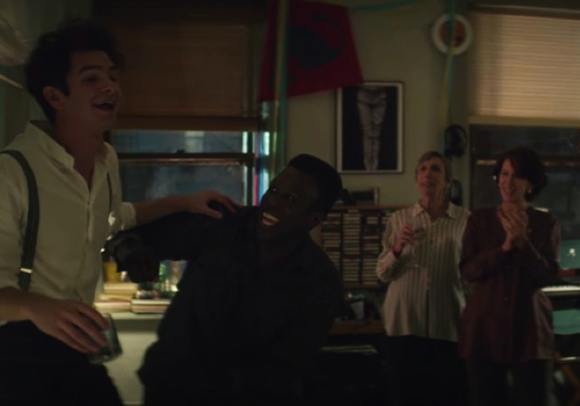 Four young adults laughing and clapping together in a dimly lit indoor setting.