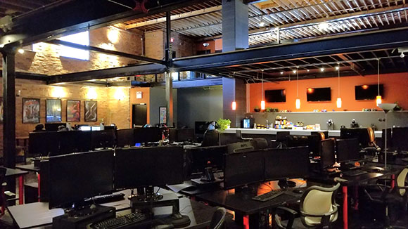 An open office interior with rows of computer monitors, desks, and chairs under industrial lighting.
