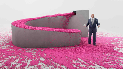 A man in a blue suit stands beside a large gray trough overflowing with bright pink pellets.