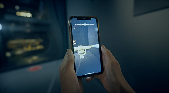 Hands holding a smartphone showing an augmented reality game with a digital cannon on screen.