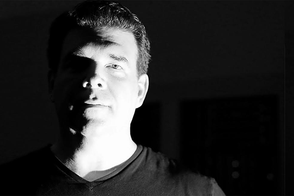 Black and white close-up portrait of a man with dramatic side lighting against a dark background.