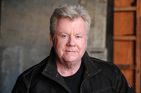 A headshot of a middle-aged man with messy light hair wearing a black jacket.