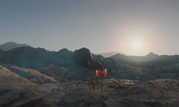 A large, dark ant-like creature stands in a rocky, mountainous desert under a bright setting sun.